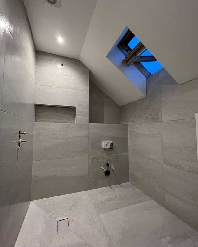 Renovated bathroom featuring grey tiles, waterproofed walk-in shower area, and natural light from skylight.